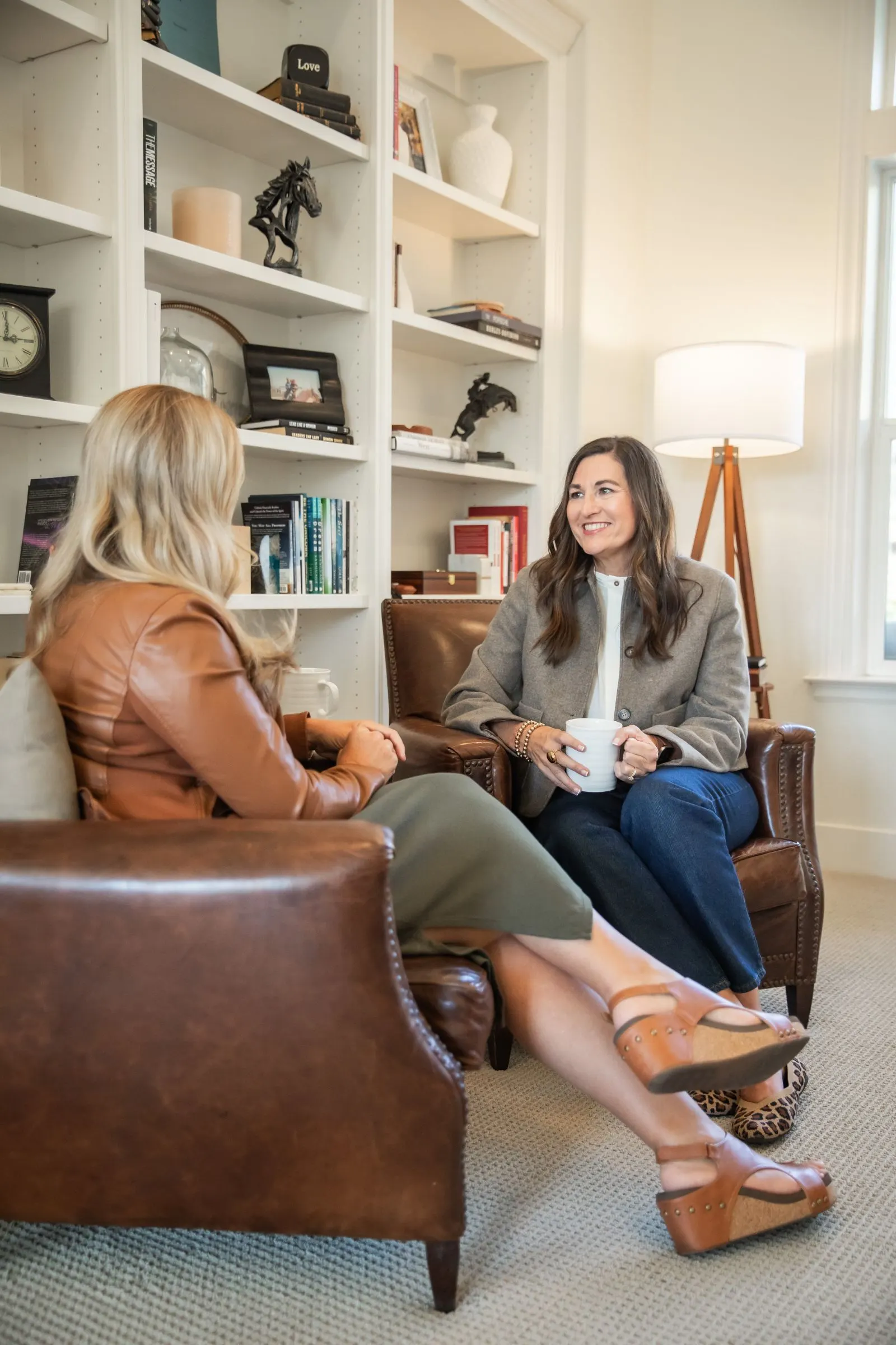 Kelly with a coffee mug, talking with a client in leather chairs
